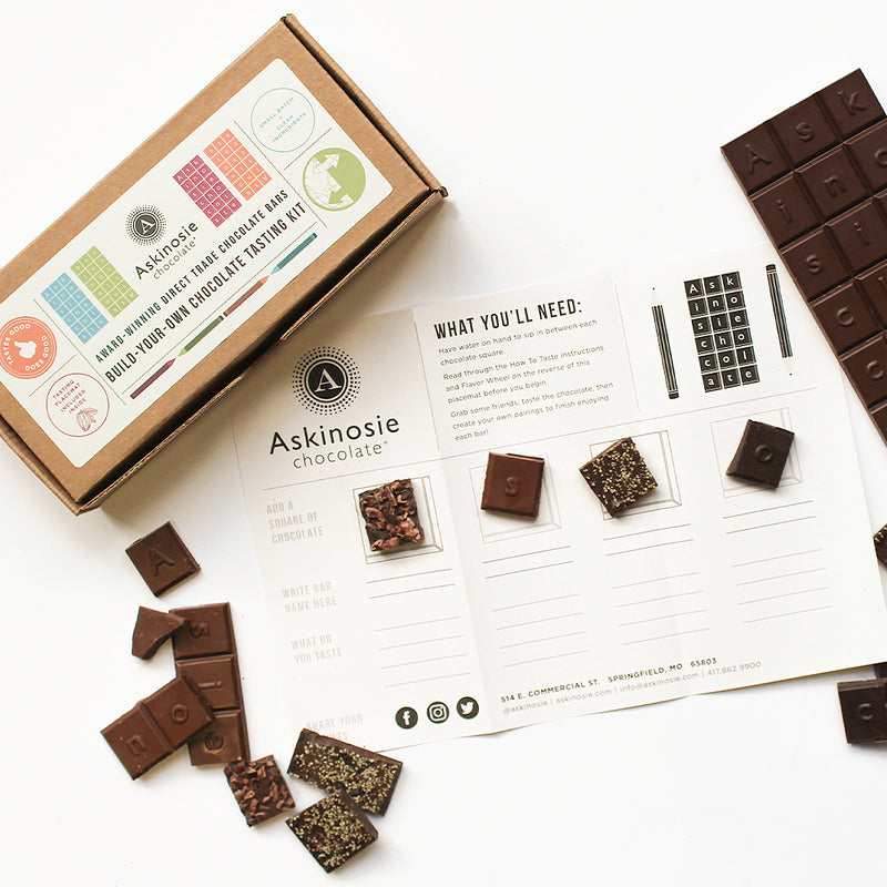 Scattered chocolate squares laid on top of a tasting placemat nearby Build Your Own Chocolate Tasting Kit packaging