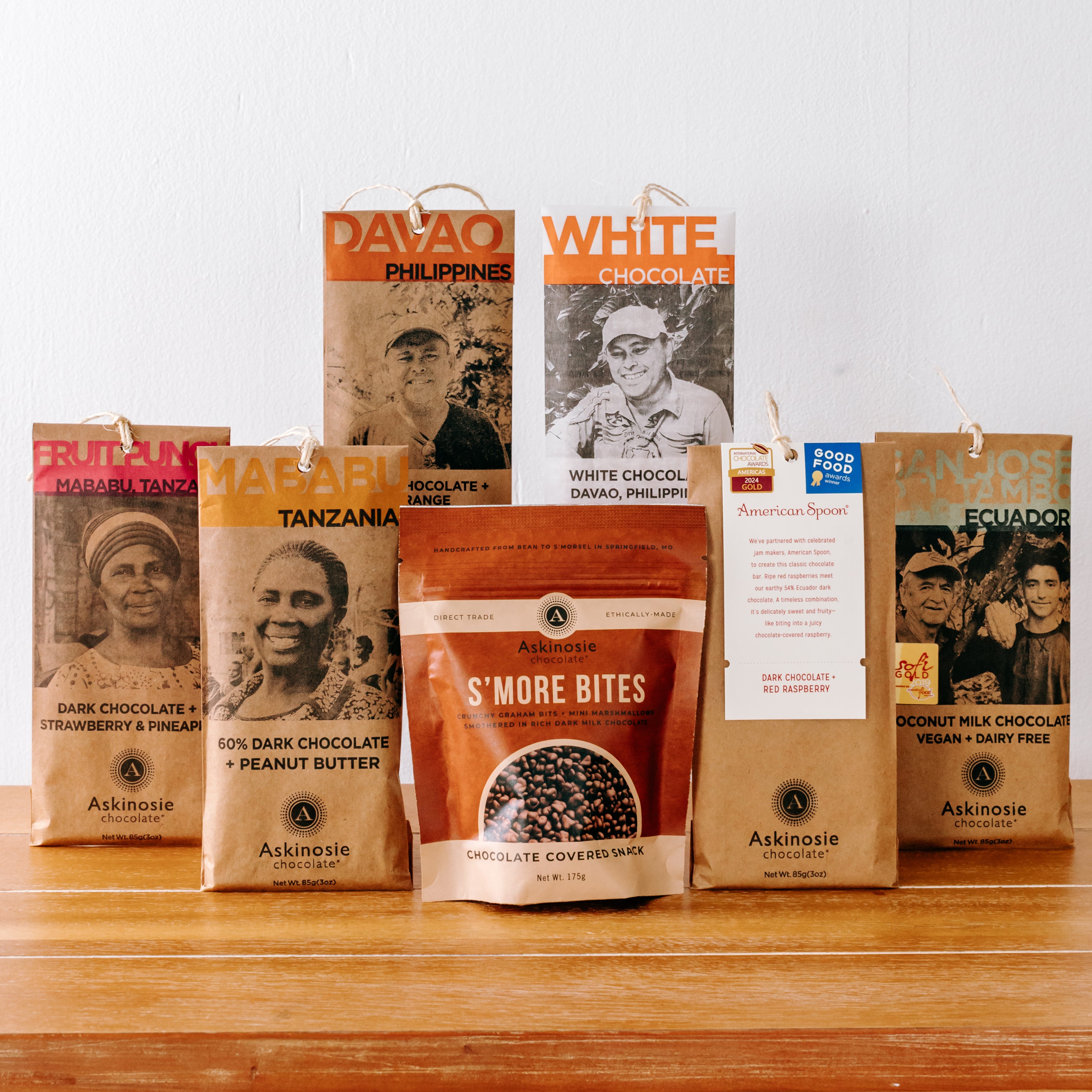 A variety of Askinosie Chocolate Bars displayed around a pouch of Chocolate Covered S'more Bites.