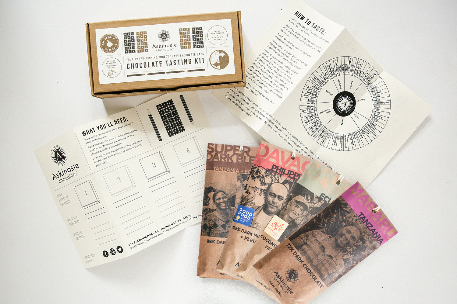 Chocolate tasting kit with kraft Askinosie Chocolate-branded packaged chocolate bars and a tasting wheel on a white background