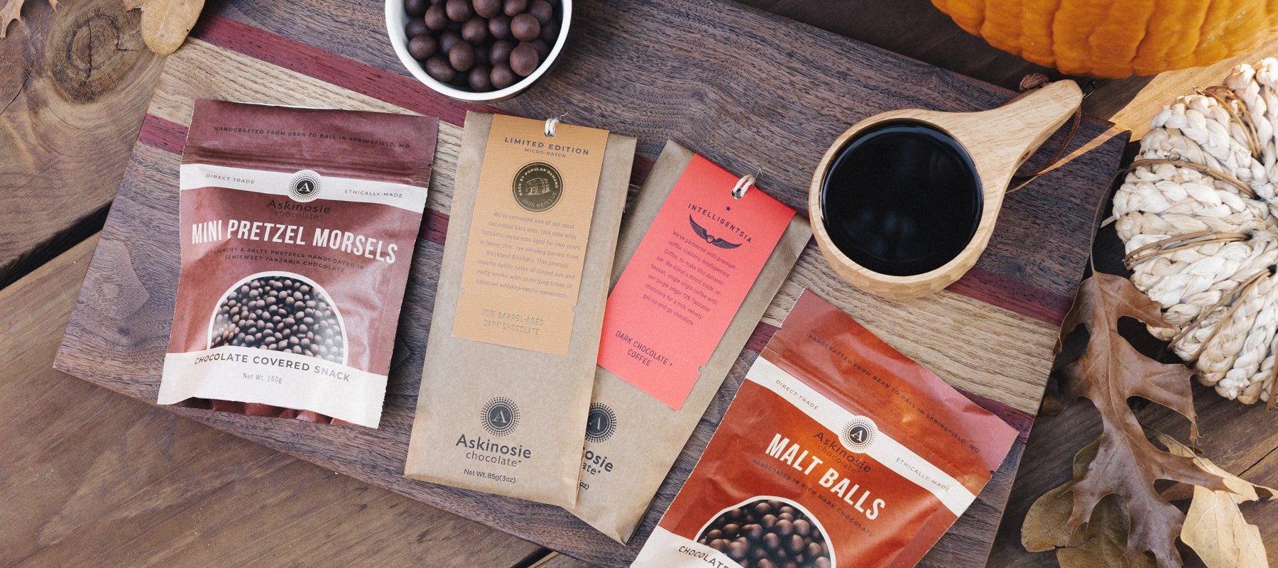 Assorted Askinosie Chocolate packages arranged on a wooden cutting board with pumpkins nearby
